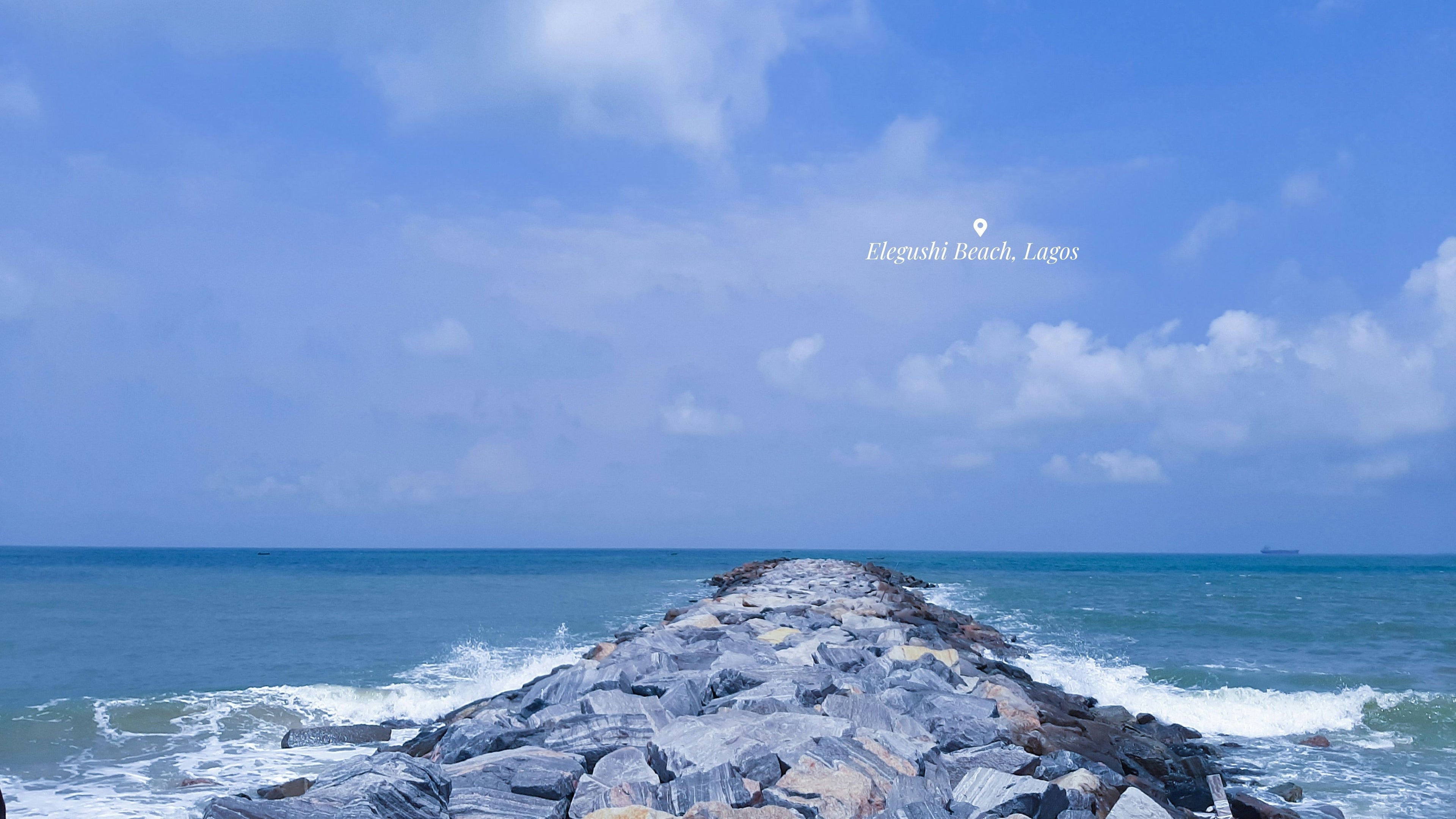 Ocean view with a rocky breakwater and clear blue sky. Elegushi Beach by Oluwatobi Babalola